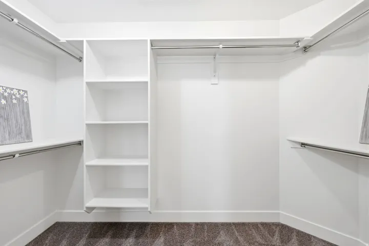 Walk-in closet featuring built-in shelving, multiple hanging rods, and dark carpeting