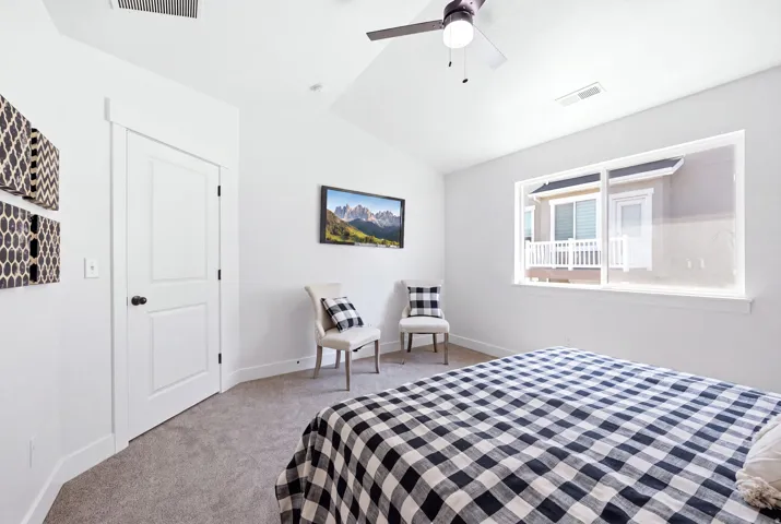 Spacious interior featuring a large window, vaulted ceiling, ceiling fan, white paneled door, and neutral-toned carpeting