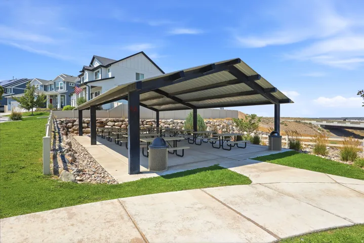Community picnic pavilion featuring a metal roof, concrete slab, multiple picnic tables, and a stone retaining wall