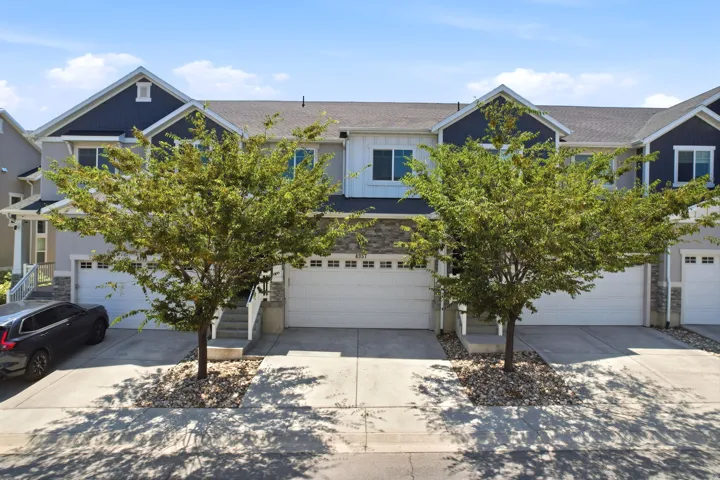 Townhome exterior featuring a combination of light-toned stucco and dark blue siding, stone veneer accents, and a two-car garage
