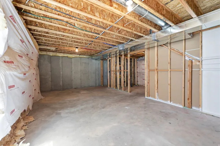 Unfinished lower level featuring exposed wood joists, concrete flooring, and partial framing for future development
