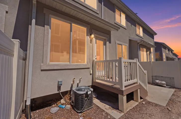 Rear exterior featuring a private deck with white railings, a concrete patio area, and a white vinyl fence