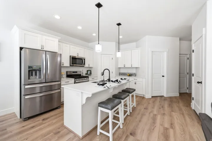 Modern kitchen featuring a central island with seating, stainless steel appliances, white cabinetry, recessed lighting, and wood-finish flooring
