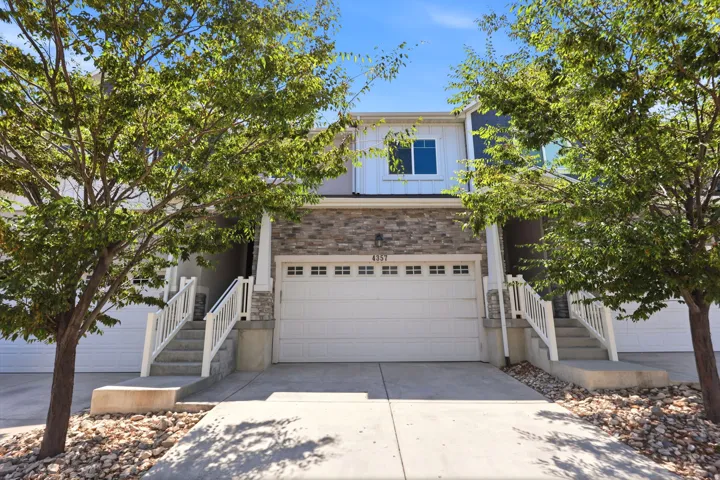 Contemporary townhouse exterior featuring a two-car garage, stacked stone accents, white siding, and a prominent entry staircase with white railings