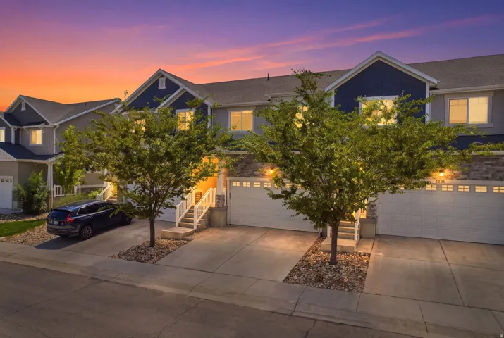 Contemporary townhome exterior featuring dual garage doors, a stone and siding facade, mature trees, and concrete driveways