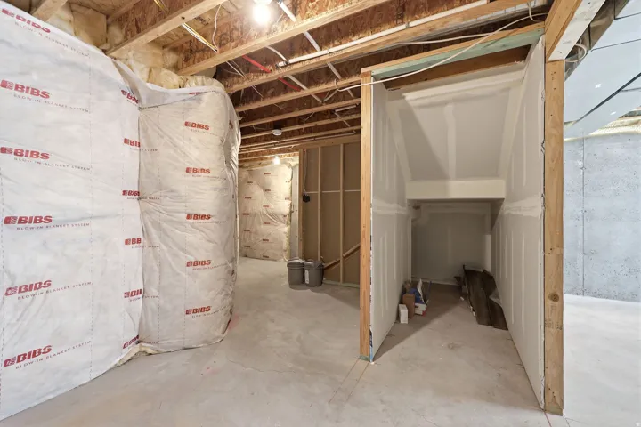 Unfinished basement space featuring visible insulation, exposed ceiling joists, concrete flooring, and framed walls