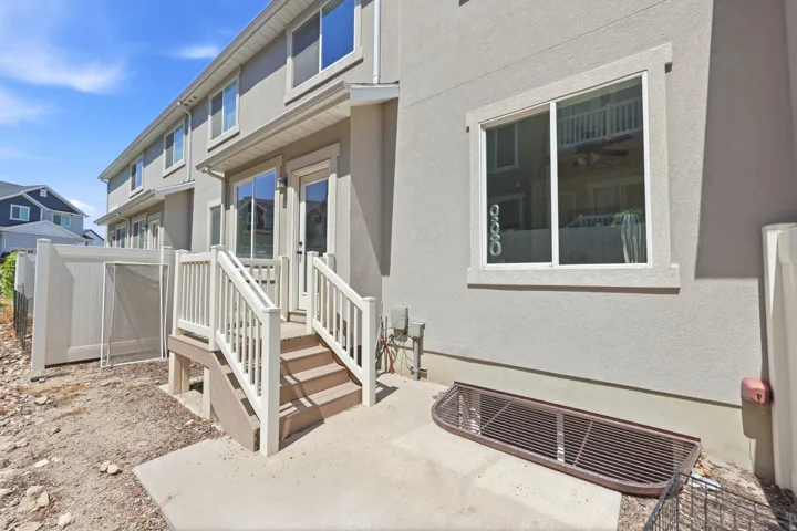 Rear exterior featuring a concrete patio, white vinyl fencing, and a deck with stairs providing access to the interior