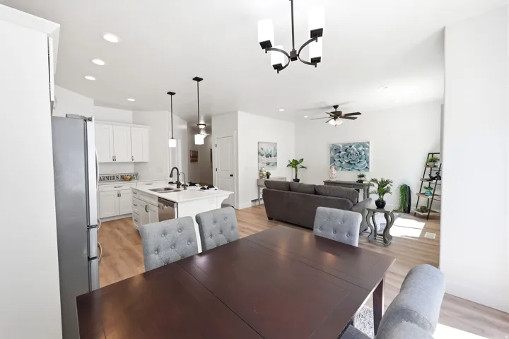 Open-concept interior featuring light wood-finish flooring, recessed lighting, and a white kitchen with an island, stainless steel appliances, and subway tile backsplash