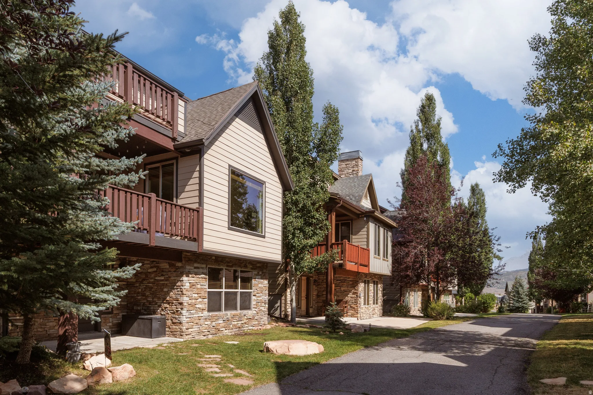 Multi-level residence featuring stacked balconies, stone veneer accents, and peaked gable on community path