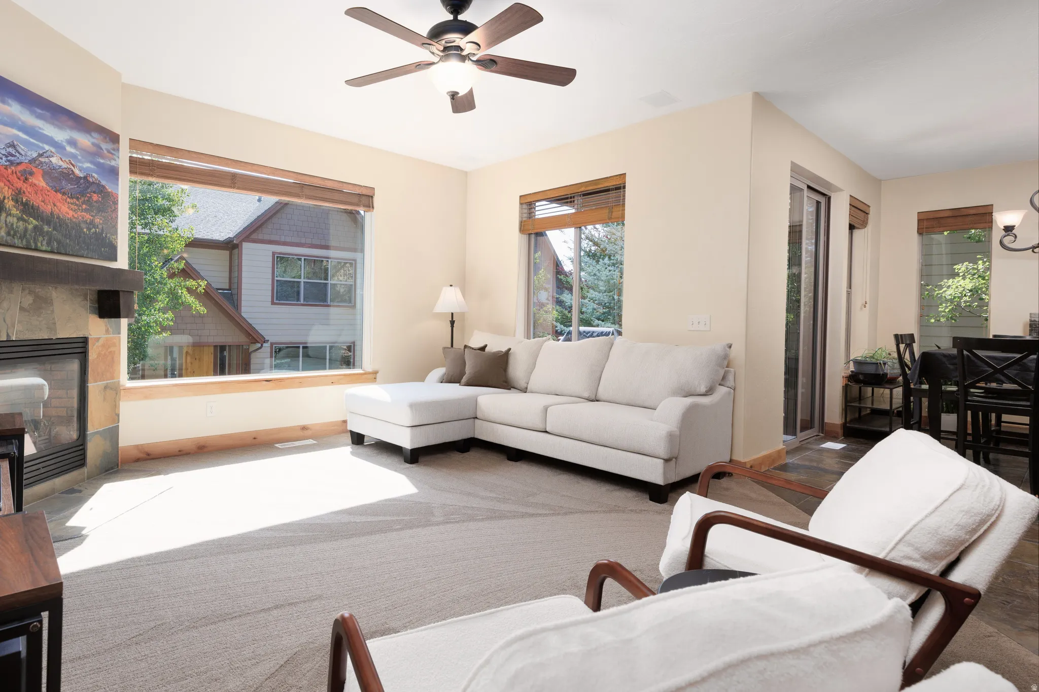 Living area featuring a ceiling fan, large windows with wood blinds, a stone-faced fireplace with a wood mantle, and a sliding glass door