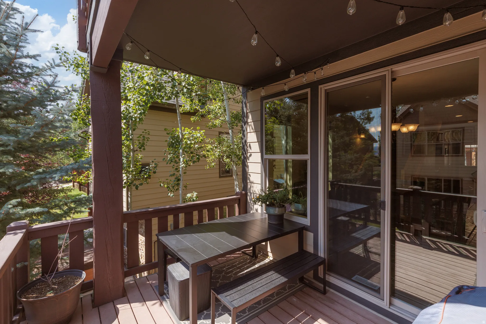 Covered outdoor deck with wood-finish flooring, dark wood railing, and a sliding glass door entry