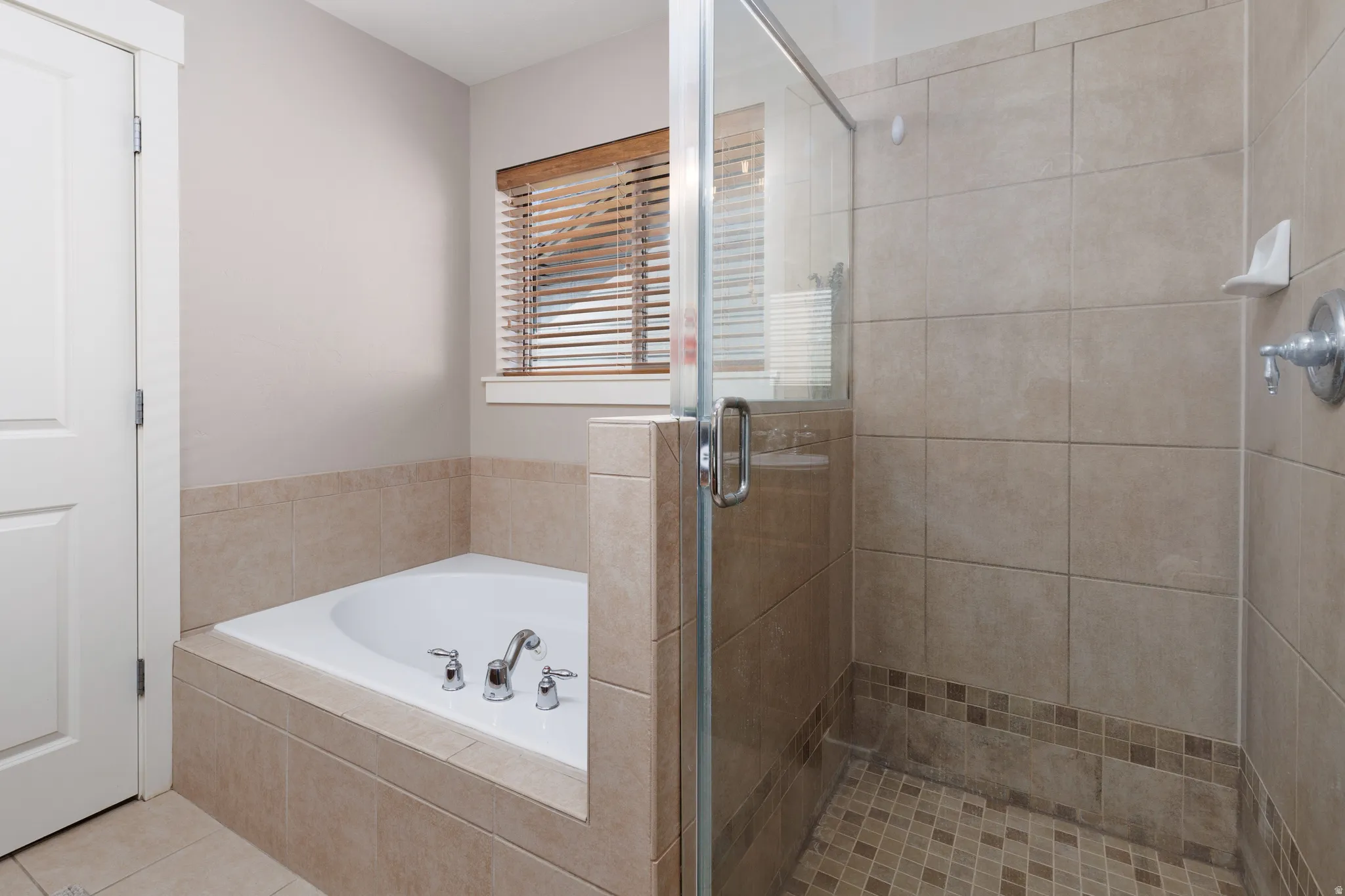 Built-in bathtub with chrome fixtures, tiled surround, and wood-finish blinds