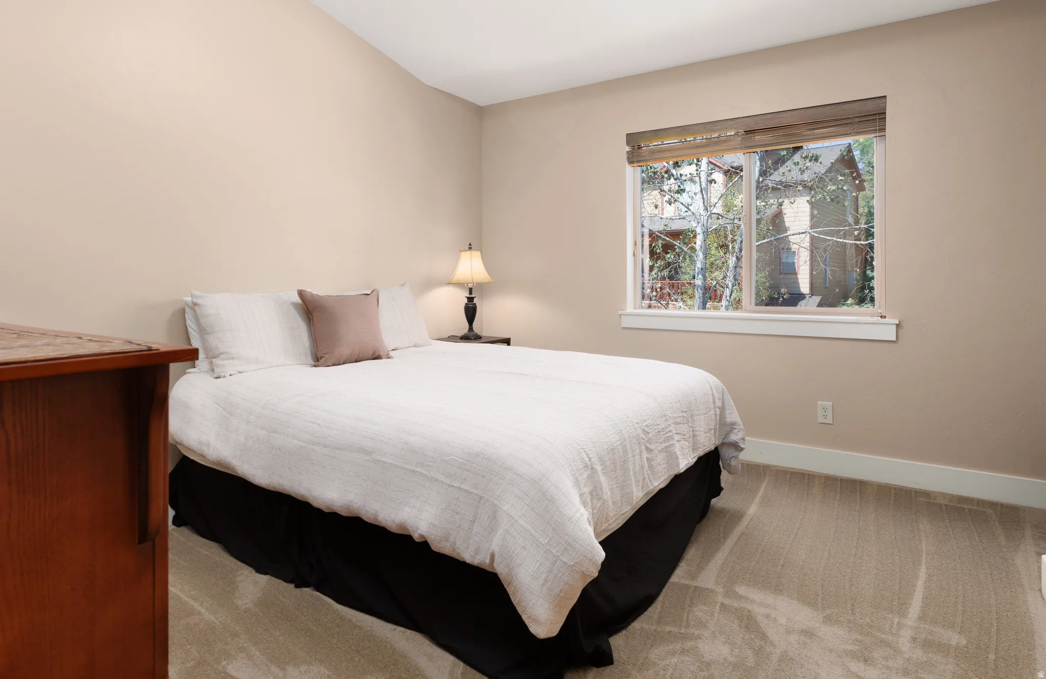 Vaulted ceiling, neutral wall paint, carpeted flooring, large window with blinds, and white trim