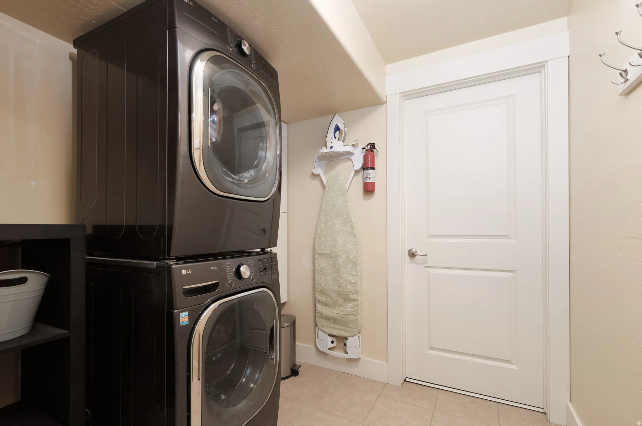 Stackable laundry appliances with a paneled interior door, complemented by light tile flooring and a neutral wall color