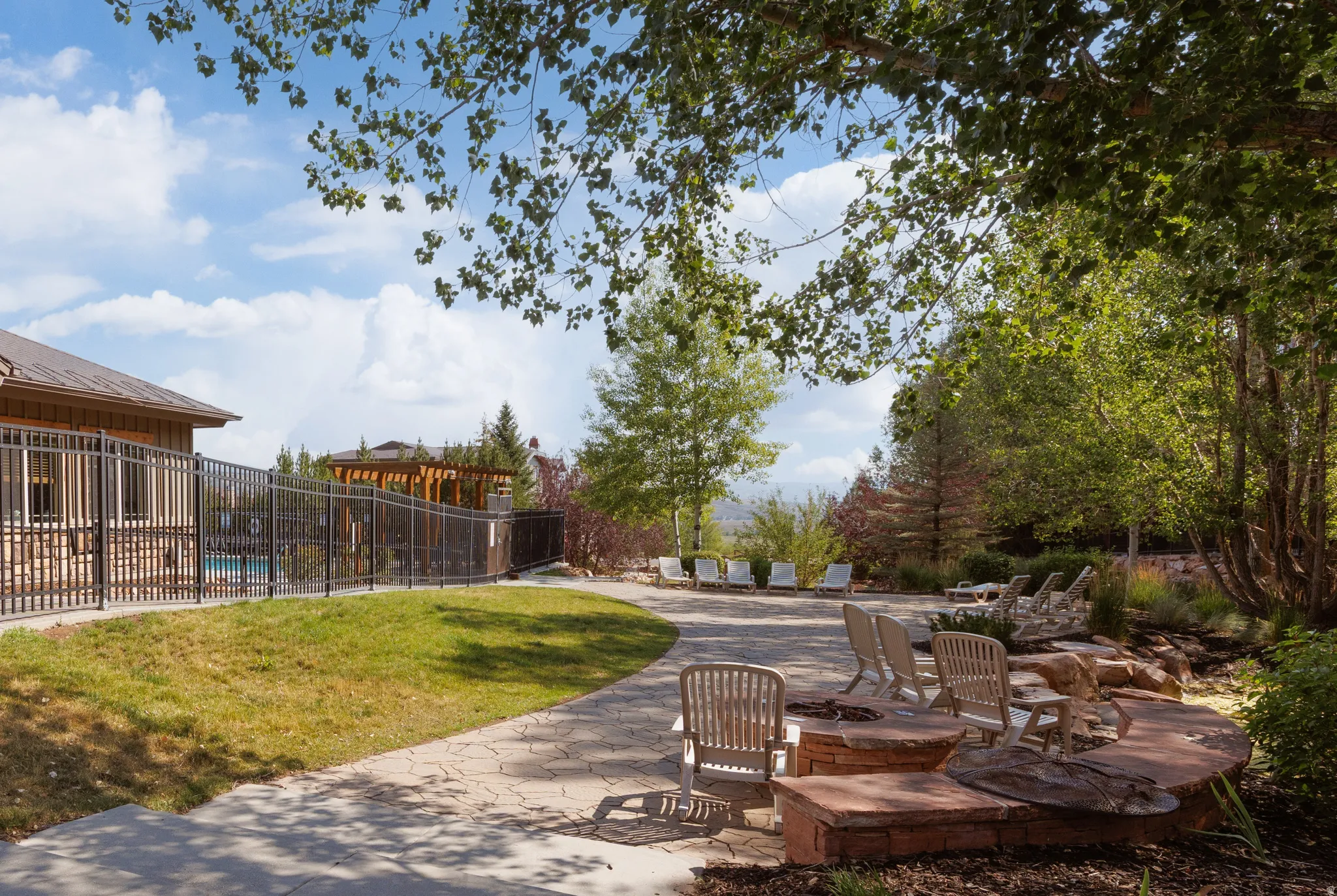Landscaped outdoor area featuring a stone pathway, a built-in fire pit with stone seating, and a perimeter fence enclosing an outdoor pool