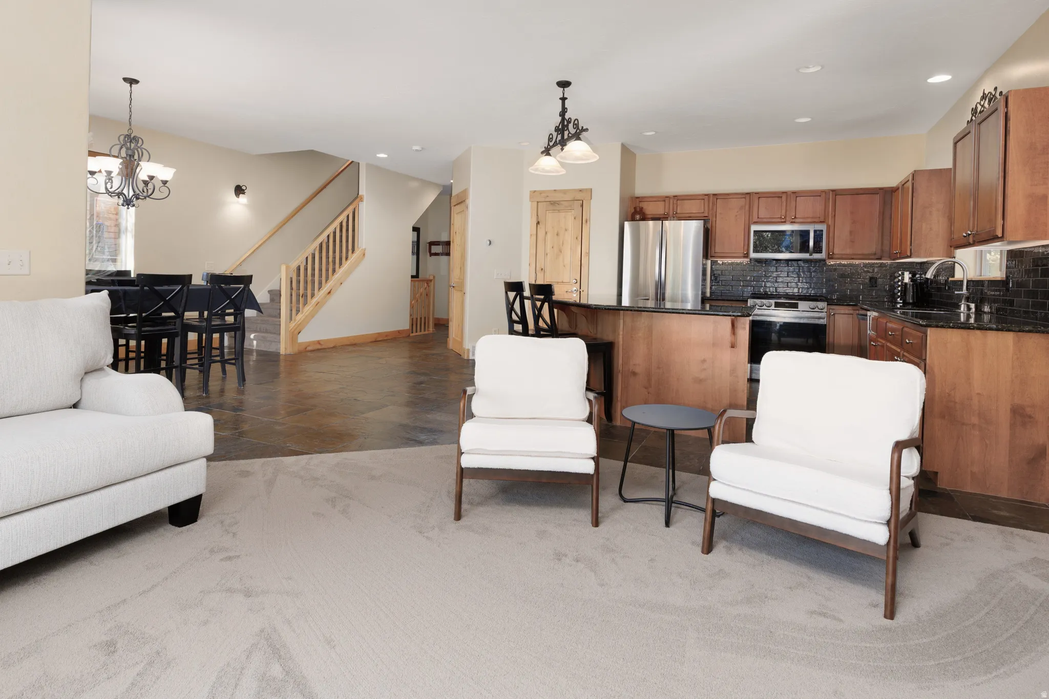 Open concept living area featuring a kitchen with wood cabinetry, stainless steel appliances, and a dark tile backsplash