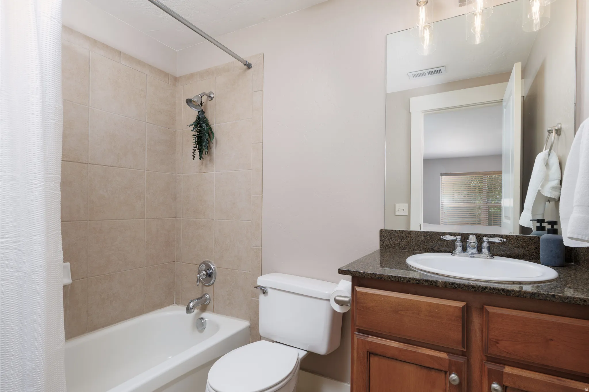 Bathroom featuring a tiled tub/shower combination, an oval undermount sink, a dark countertop, and a wood-finish vanity