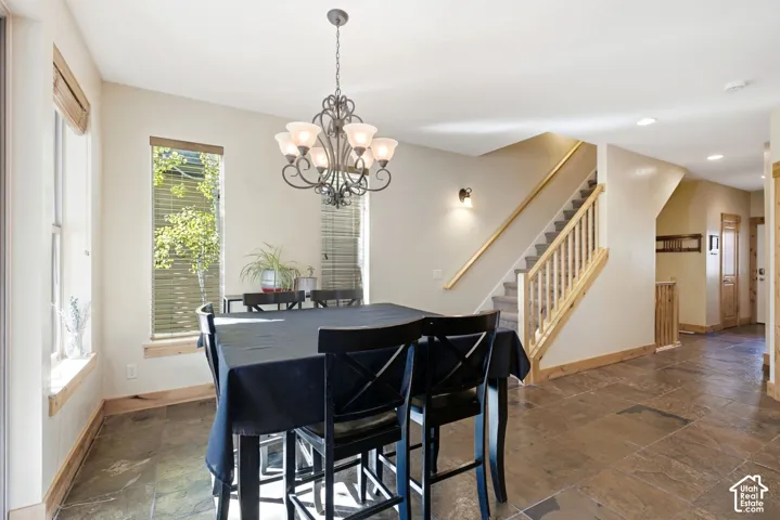 Dining area with a wrought iron chandelier, large windows, tile flooring, and a staircase with wood railings and carpeted treads