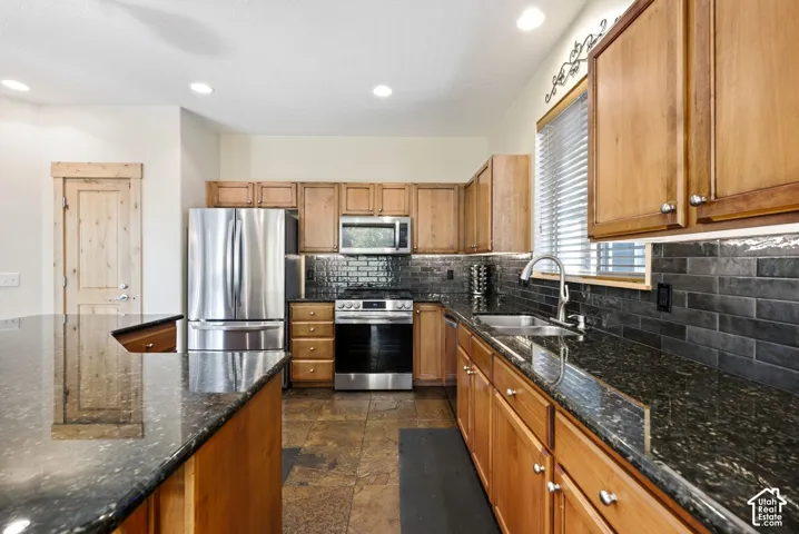 Kitchen featuring dark granite countertops, stainless steel appliances, wood cabinetry, a dark subway tile backsplash, and recessed lighting