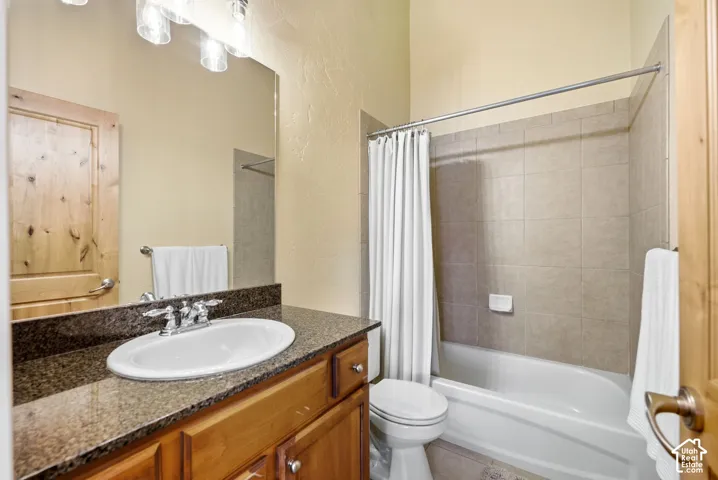 Vanity with a polished chrome faucet and an oval basin, wood cabinetry, stone countertop, tile flooring, and a tiled shower-tub combination