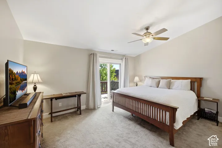 Vaulted ceiling with a ceiling fan, sliding glass door, private balcony with railing, and light-toned carpeting