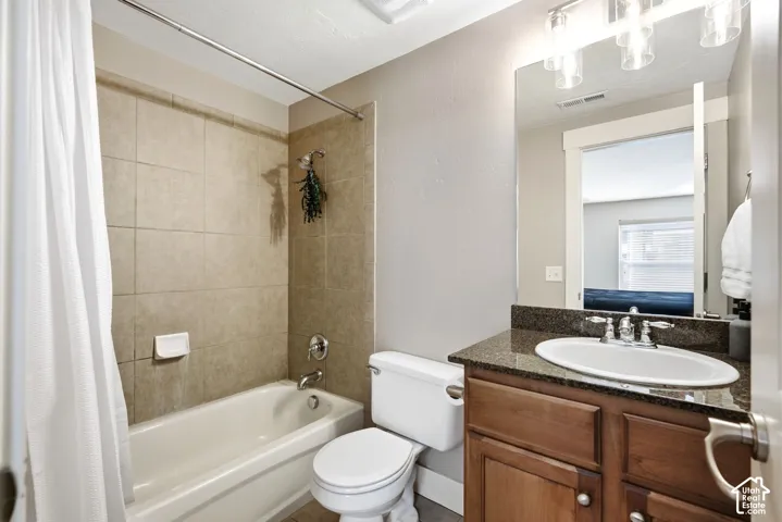 Tub/shower combination with tile surround, wood-finish vanity with an undermount sink, and a dark stone-finish countertop
