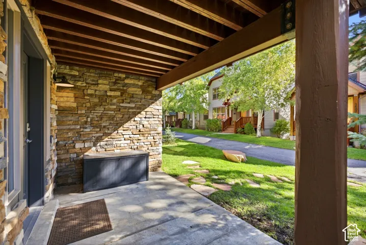 Stone veneer exterior with a covered concrete patio, wood beam ceiling, and a paver stone walkway