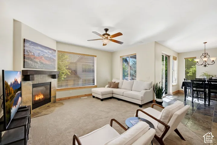 Spacious living area featuring a stone-faced fireplace with a wood mantel, a ceiling fan, and large windows