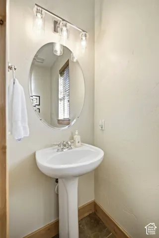 Pedestal sink with chrome faucet, oval mirror, and three-bulb vanity light fixture