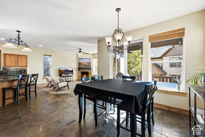 Open concept living space featuring stone-finish flooring, a dining area with an ornate chandelier, and a living area with a stone-surround fireplace