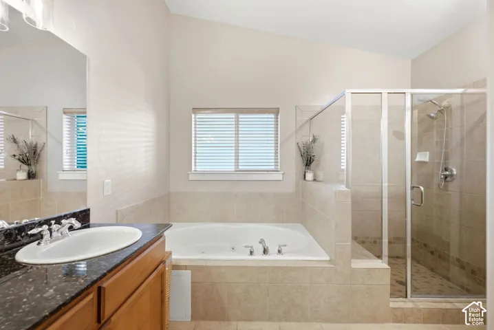Soaking tub, glass-enclosed shower, wood-finish vanity with countertop, and a window with blinds