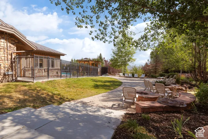 Expansive stone paver patio featuring a stone fire pit, wood-look chairs, stream, and lush landscaping