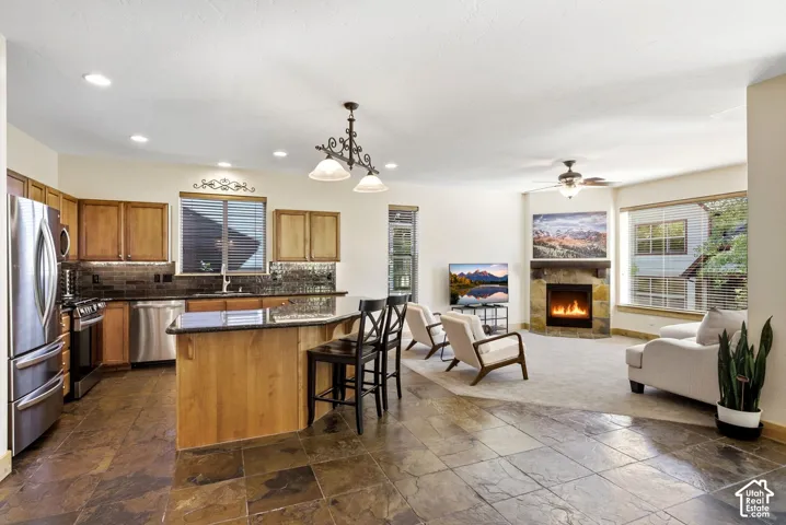 Spacious open-concept living area featuring stone tile flooring, a kitchen island with seating, recessed lighting, and a stone-faced fireplace