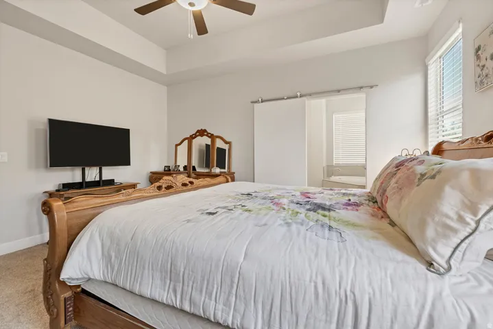 Tray ceiling with a ceiling fan, light-toned walls, barn door entry, and window with blinds