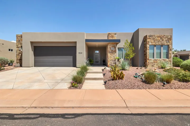 Contemporary stucco exterior with natural stone accents, a modern garage door, desert landscaping, and a covered entryway