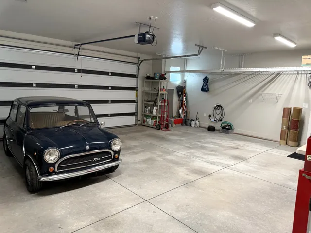 Spacious garage with overhead storage racks, an automatic garage door opener, and multiple wall-mounted electrical outlets