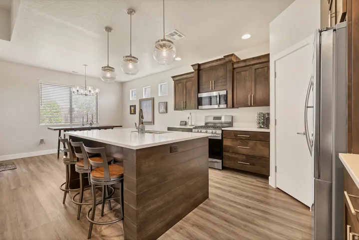 Kitchen featuring a large island with a light-toned countertop, wood-finish flooring, dark wood cabinetry, stainless steel appliances, and pendant lighting