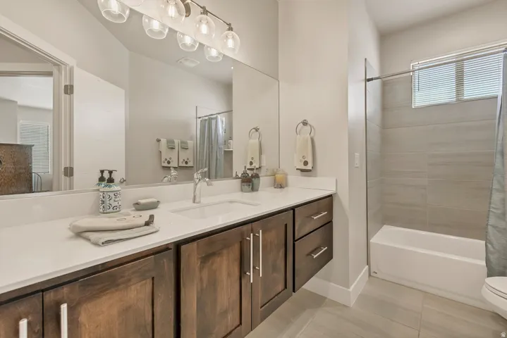 Dual-sink vanity with wood-finish cabinetry, white countertop, and contemporary light fixture