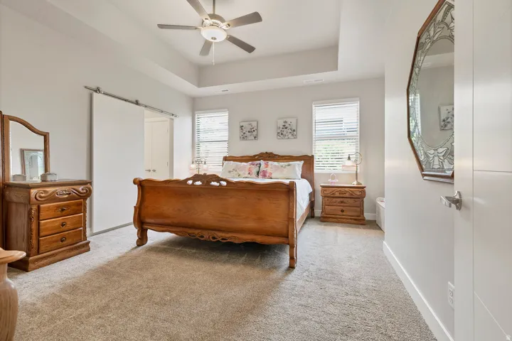 Recessed ceiling with a central fan light fixture, light gray carpeting, and a white sliding barn door