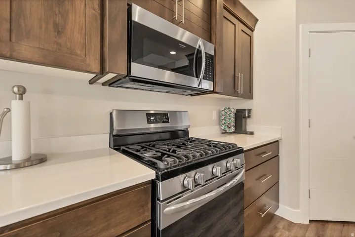 Stainless steel range with a built-in microwave, wood-finish cabinetry with brushed nickel pulls, and white countertops