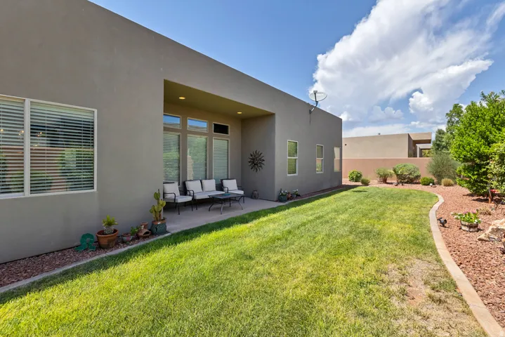 Private covered patio with recessed lighting, expansive lawn, and mature landscaping with rock detailing