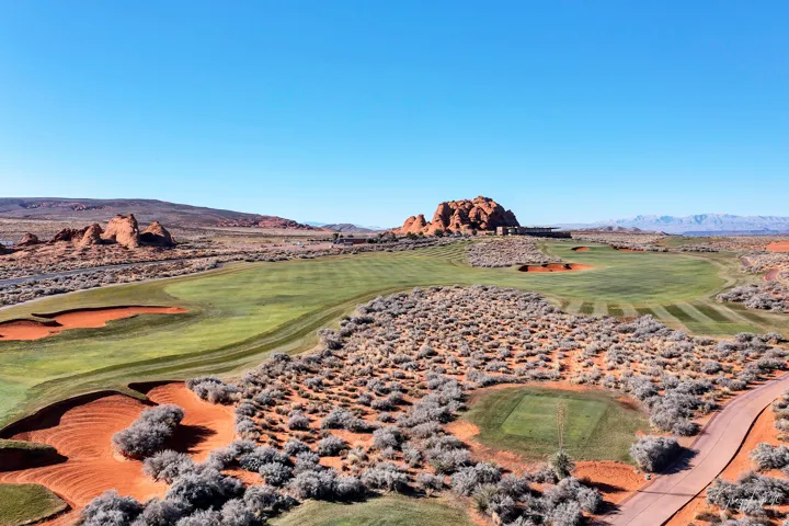 Desert landscape featuring a golf course with red sand traps and green fairways, surrounded by natural rock formations and distant mountains