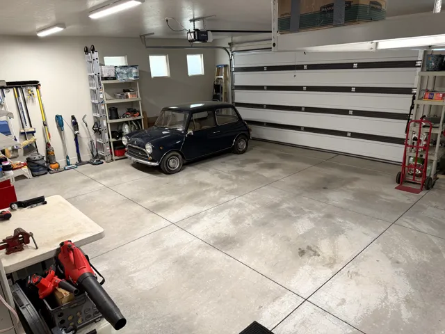 Concrete flooring, overhead garage door, built-in wall shelving, three upper windows, and overhead lighting fixtures
