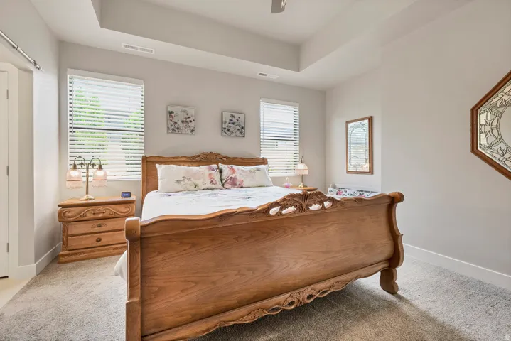 Room featuring a tray ceiling, two windows with horizontal blinds, and carpeted flooring