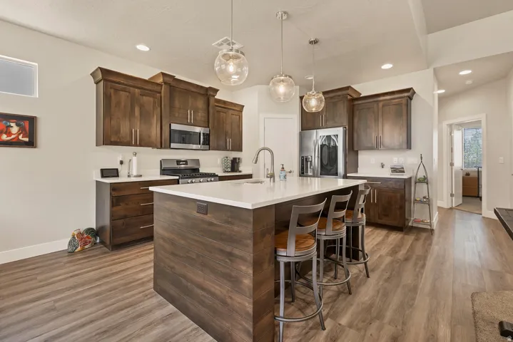 Kitchen featuring wood-finish flooring, dark wood cabinetry, white countertops, stainless steel appliances, and a large island with pendant lighting