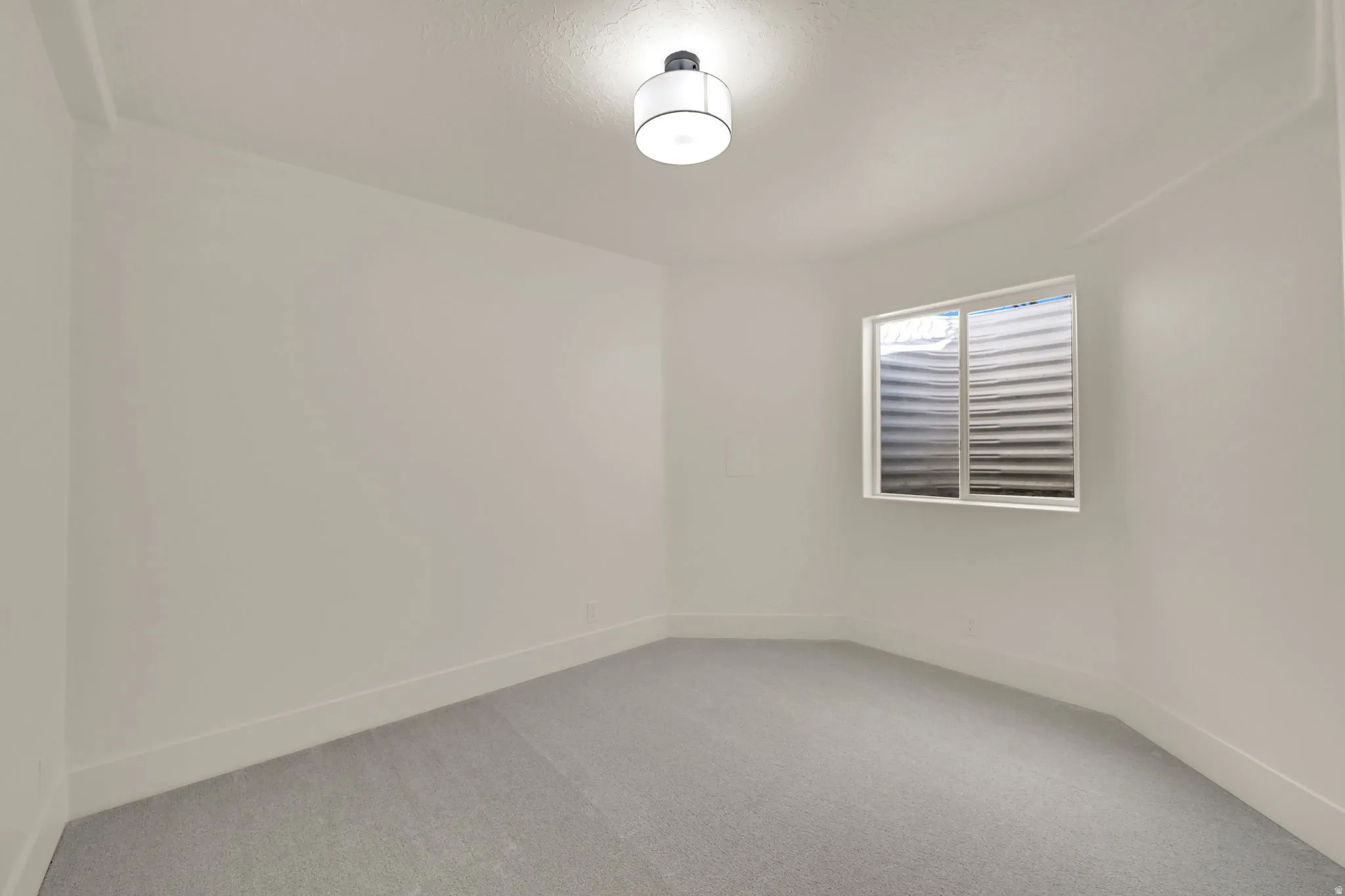 Neutral wall paint, light-colored carpet, window with horizontal blinds, flush mount ceiling light fixture