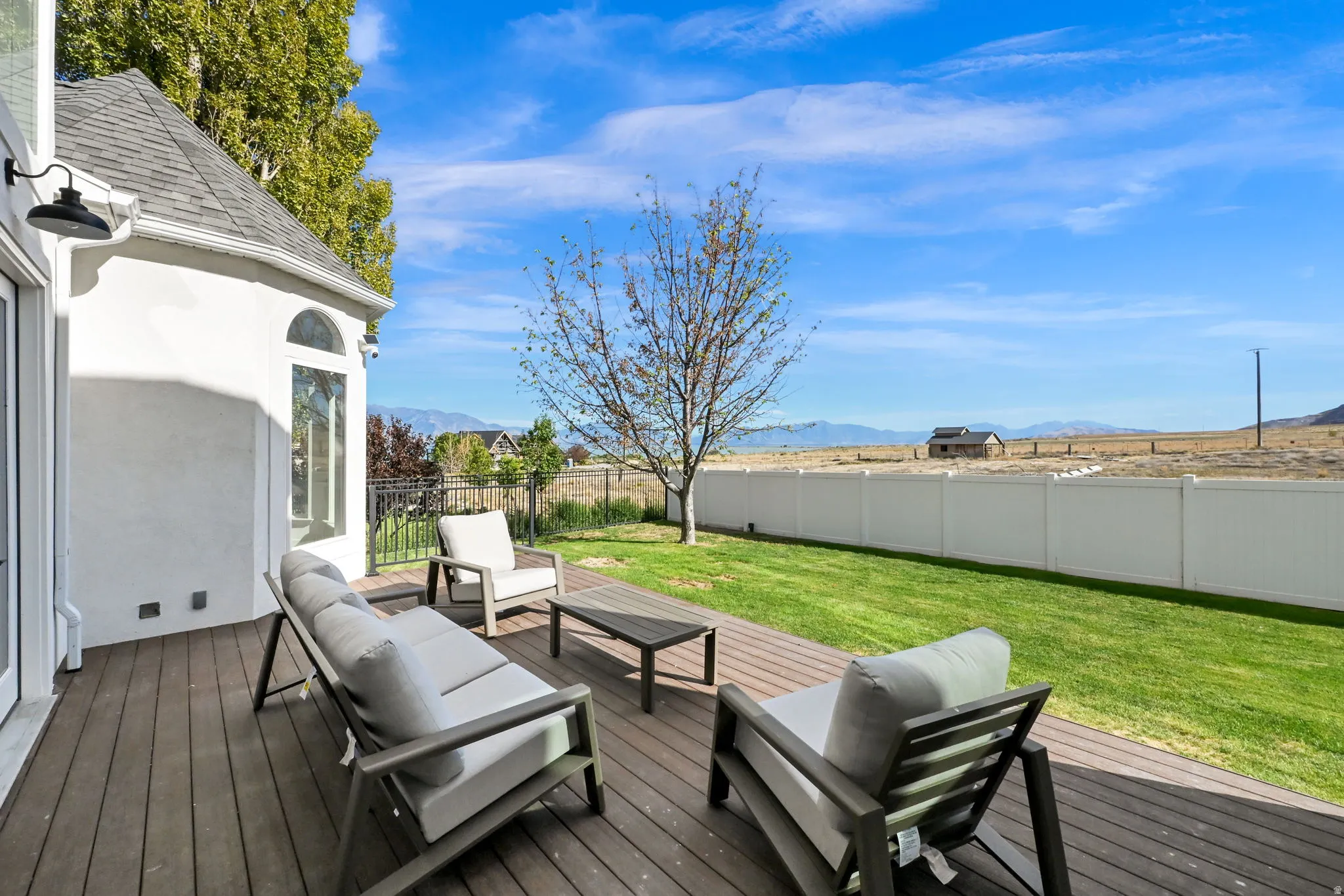 Expansive wood-finish deck, manicured lawn, white privacy fence, arched window, and exterior lighting fixture