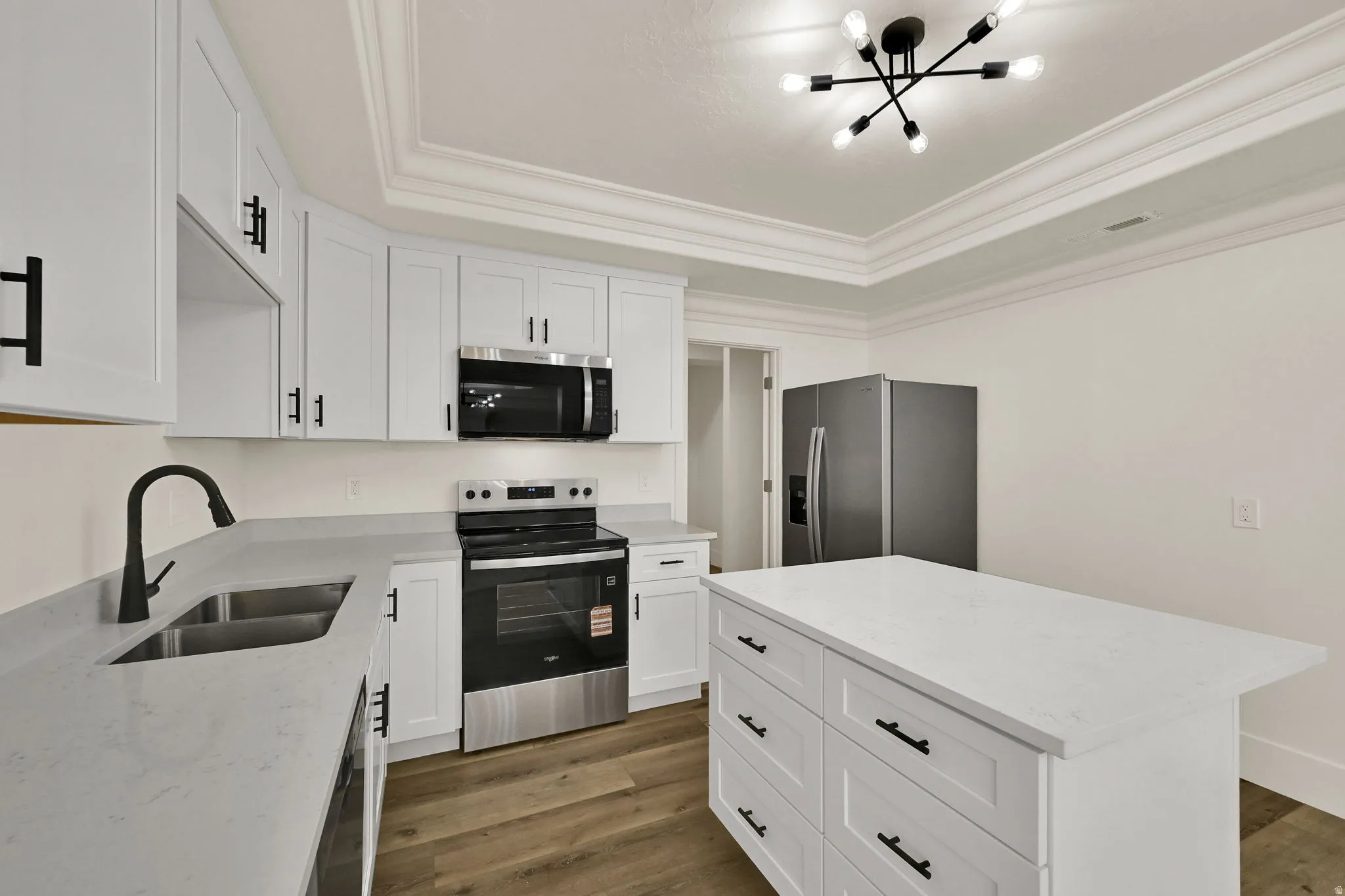 Kitchen featuring white cabinetry, stone-finish countertops, stainless steel appliances, a center island with storage, and wood-finish flooring