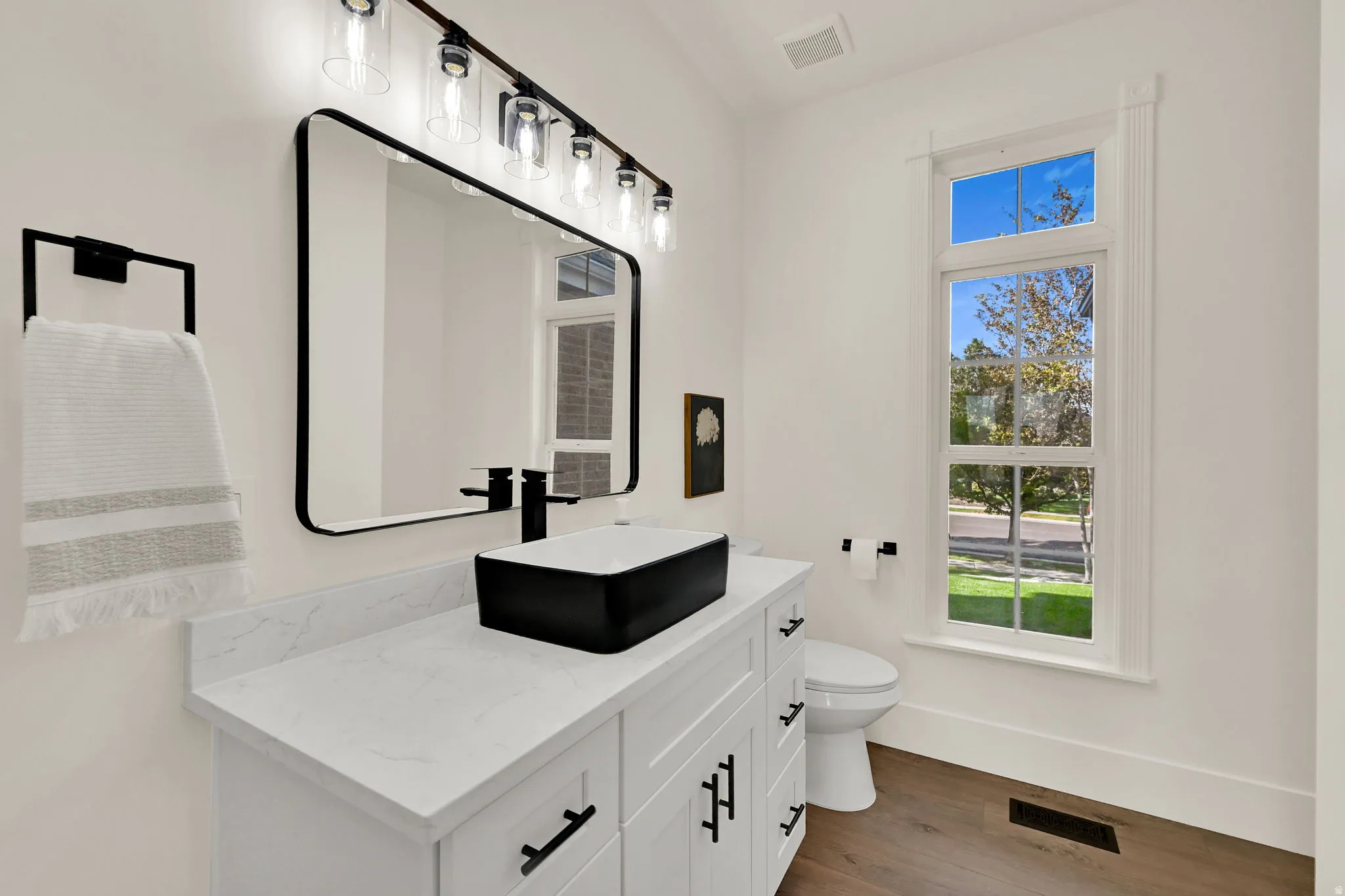 White vanity with a rectangular black vessel sink, black wall-mounted faucet, and a large framed mirror with overhead lighting