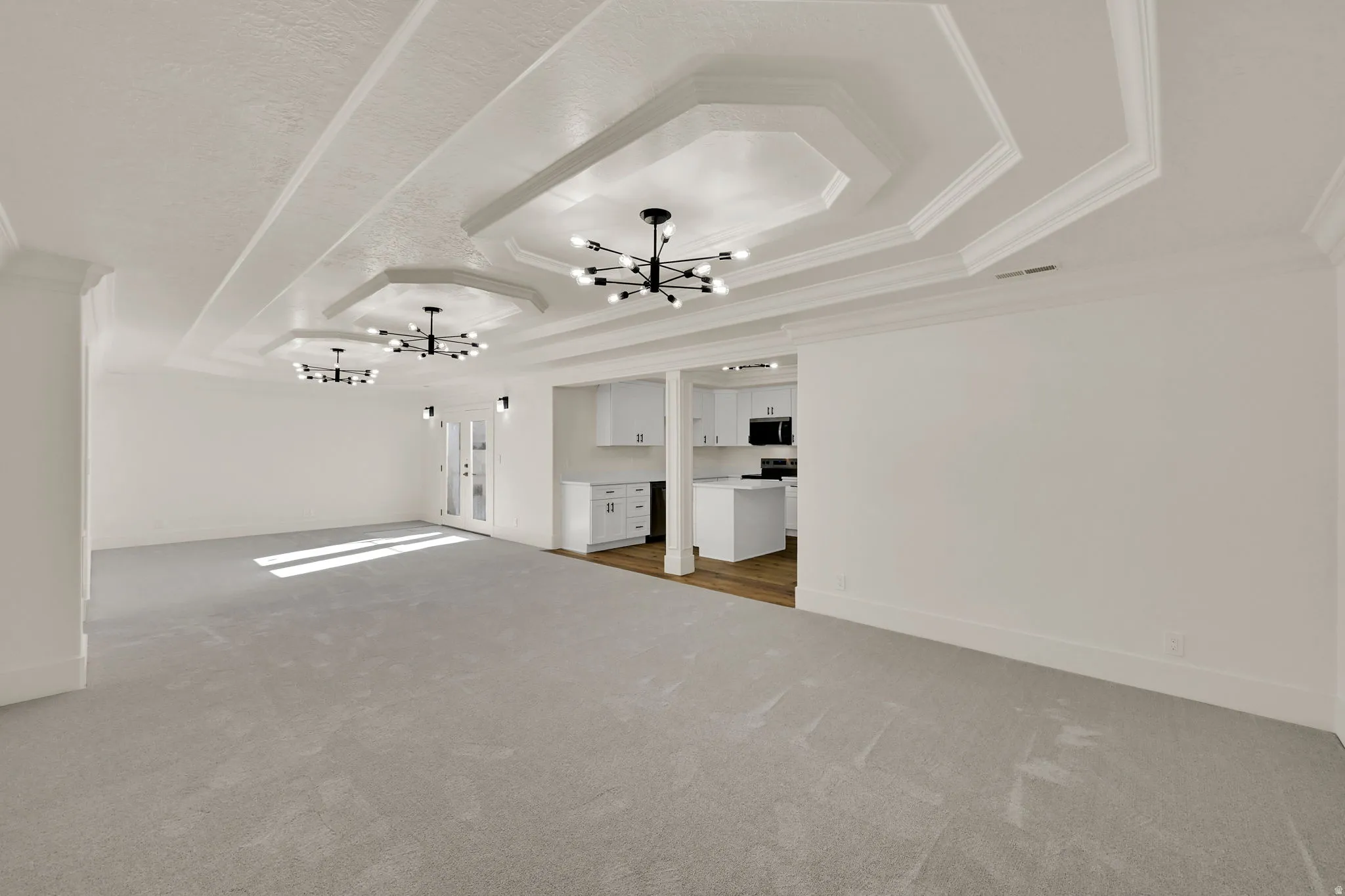 Recessed hexagonal ceiling details, contemporary black chandeliers, light-toned carpeting, white cabinetry, and wood-finish flooring